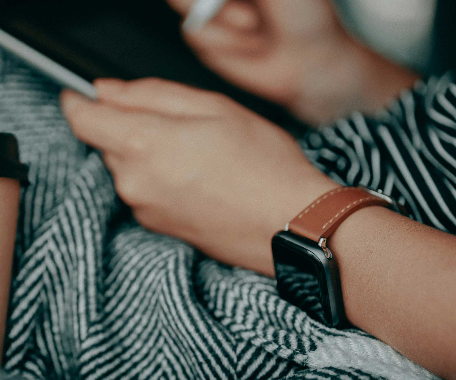 A lifestyle image of a female wearing a Apple Watch on a brown genuine leather watch strap.