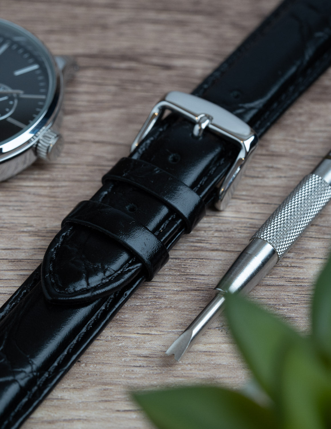 A close up image of a crocodile grain black leather watch strap.