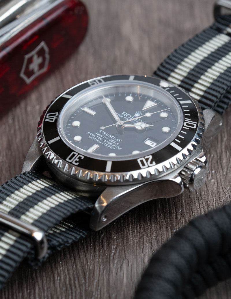 A close up image of a Rolex Sea Dweller with a black and grey Bond NATO watch strap fitted.