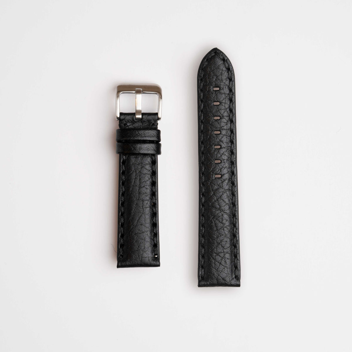 A premium black leather watch strap, showcasing its distinctive hand-stitching with prominent, oversized thread. Complete with a sleek buckle, the strap is elegantly laid out against a white background.