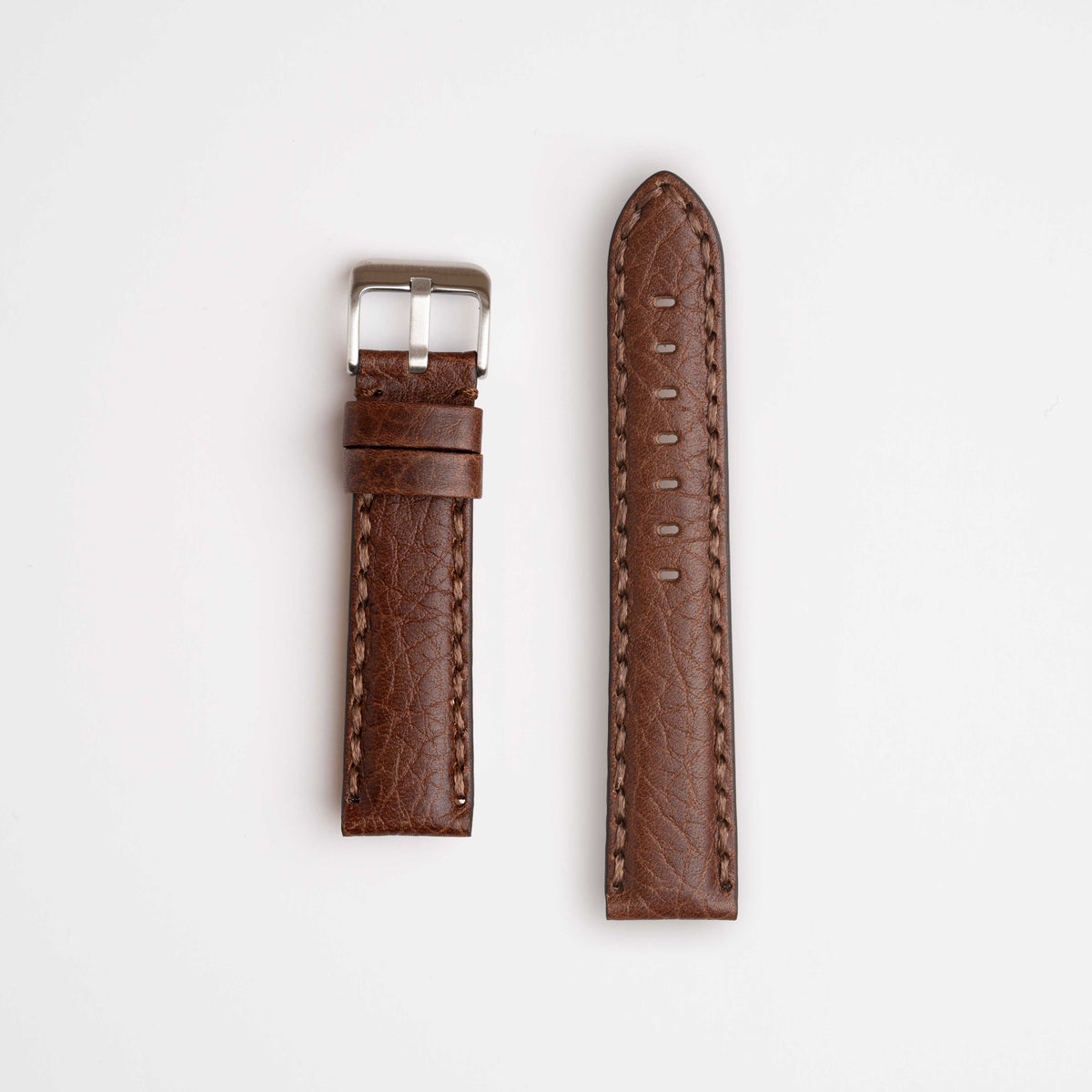 A rich brown leather watch strap, beautifully showcasing its distinctive hand-stitching with prominent, oversized thread. Complete with a sleek buckle, the strap is elegantly laid out against a white background.